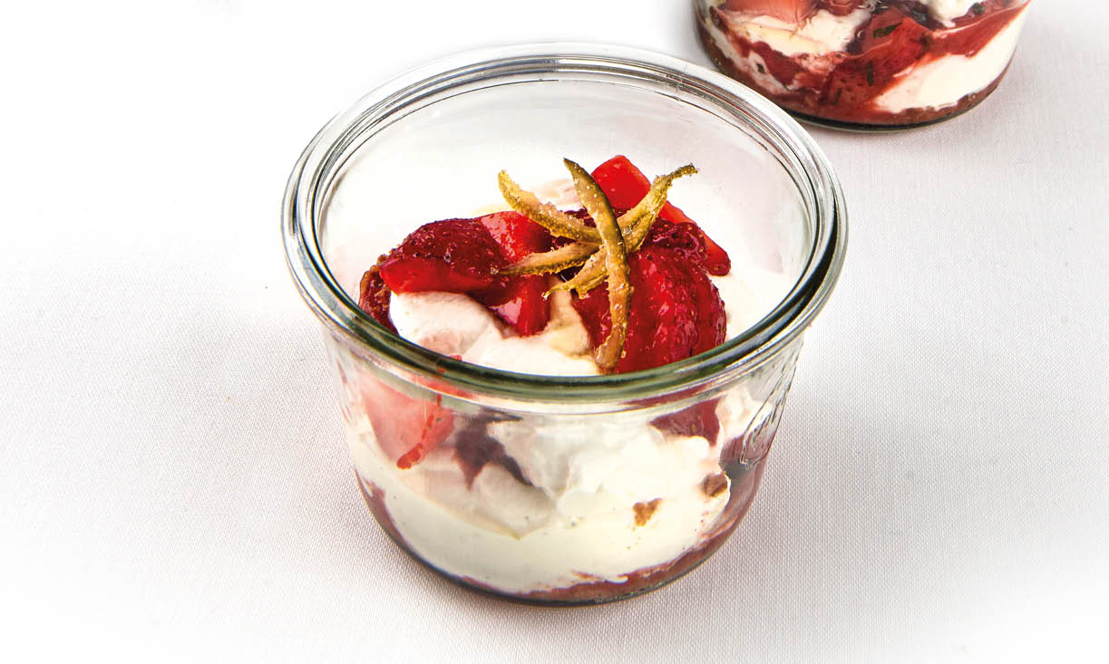Aardbeienbiscuit geserveerd in een glas, met honingcrumble en vanilleslagroom